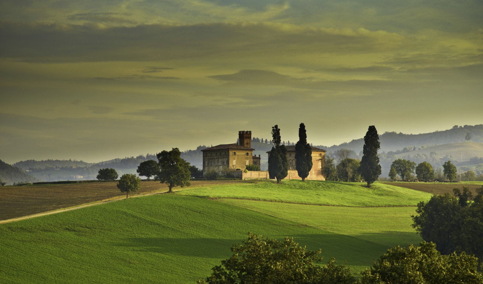 A medieval castle and cypress trees rising above an estate lawn in Tuscany