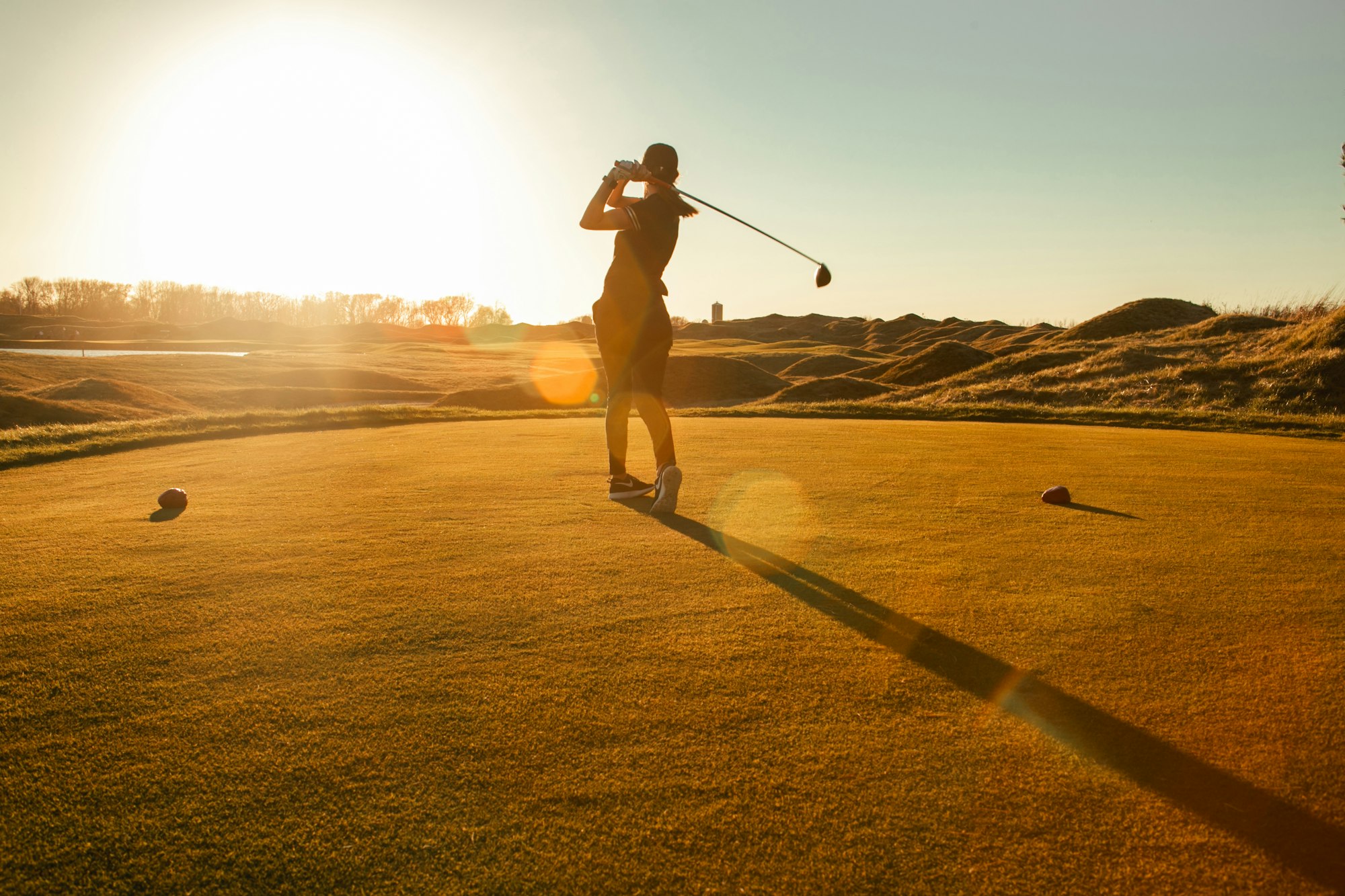 A golfer driving off the tee at sunrise on a links course, driver high at the top of the swing