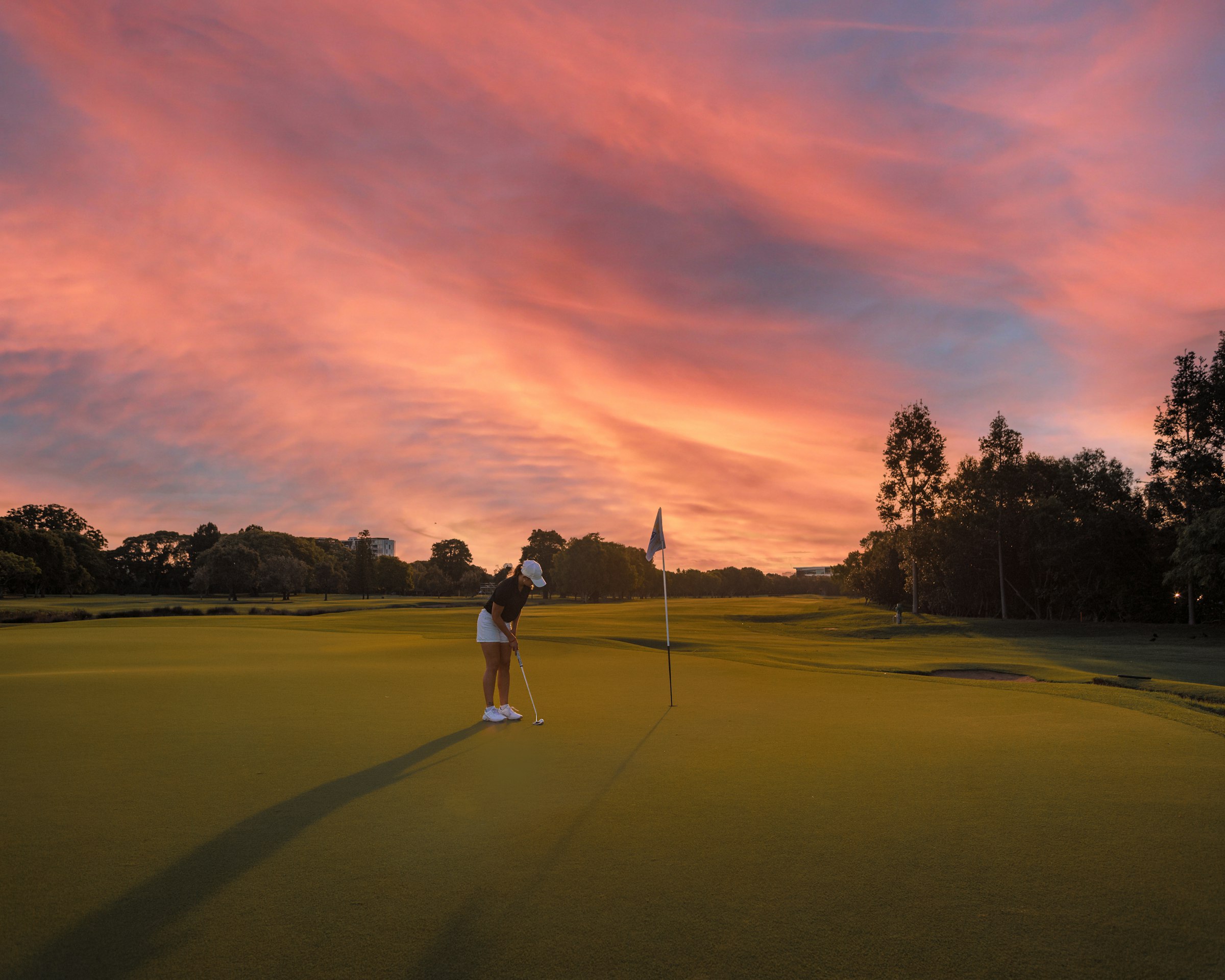 A golfer putting on a quiet green at sunset, framed by Italian umbrella pines